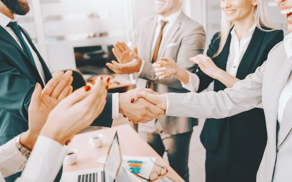 Business partners shaking hands while other colleagues clapping. 