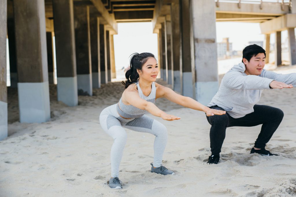 A couple is doing squats on the beach