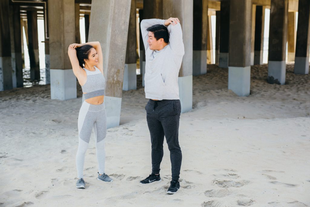 A happy couple in workout attire stretching on the beach