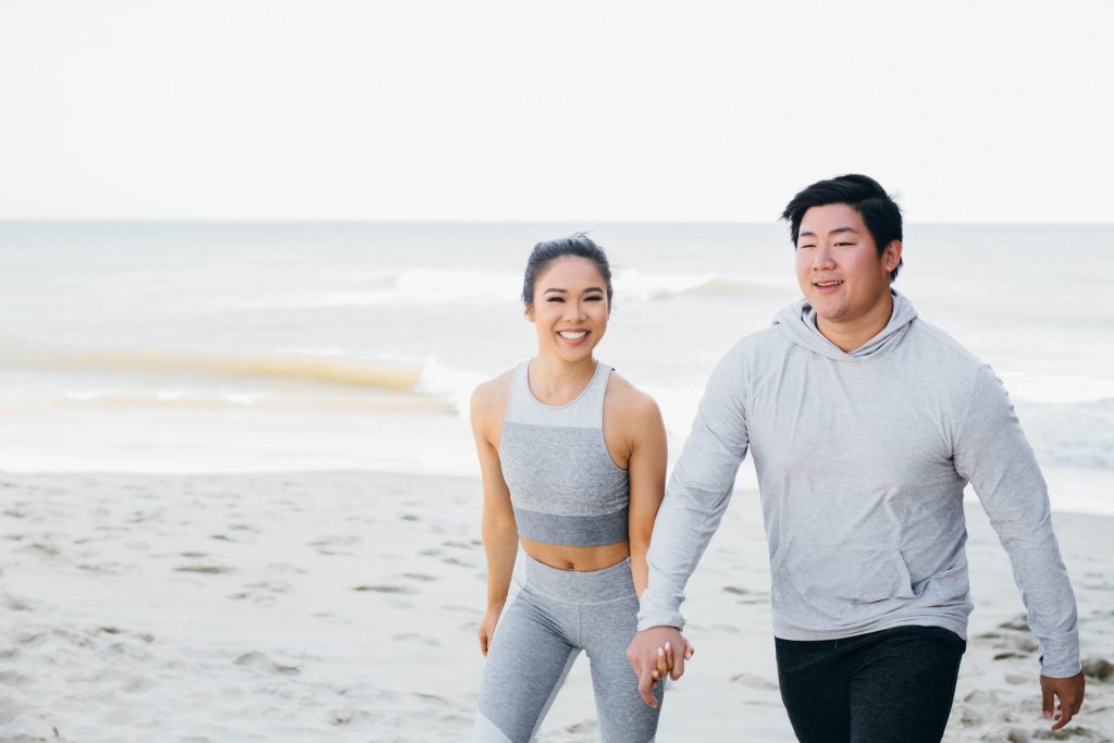 A woman and man walking hand-in-hand on the beach in workout clothes