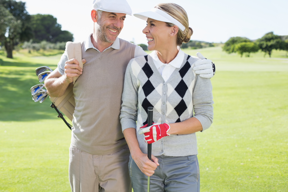 Golfing couple smiling at each other on the putting green on a sunny day at the golf course