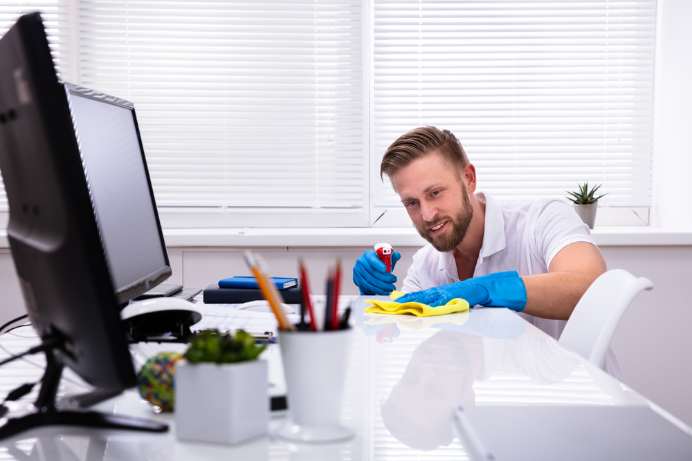 A man wearing blue gloves is wiping down his white modern desk