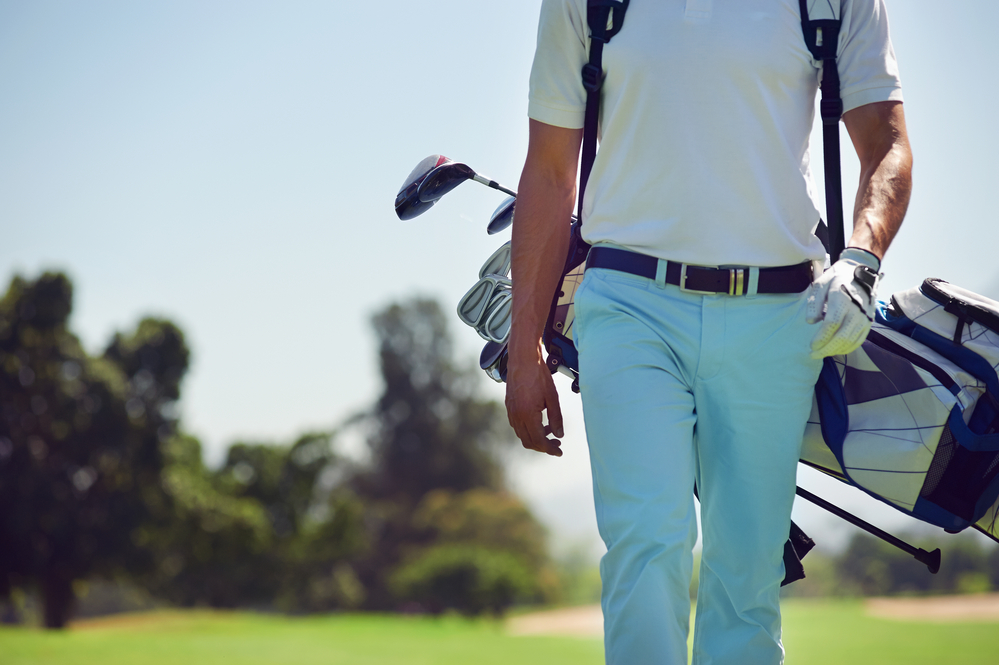 Golf player walking and carrying bag on course during