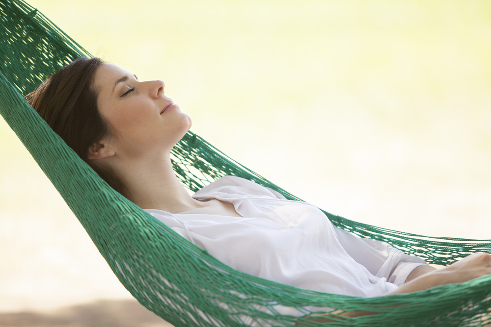 A woman is taking a nap in a hammock by the shore