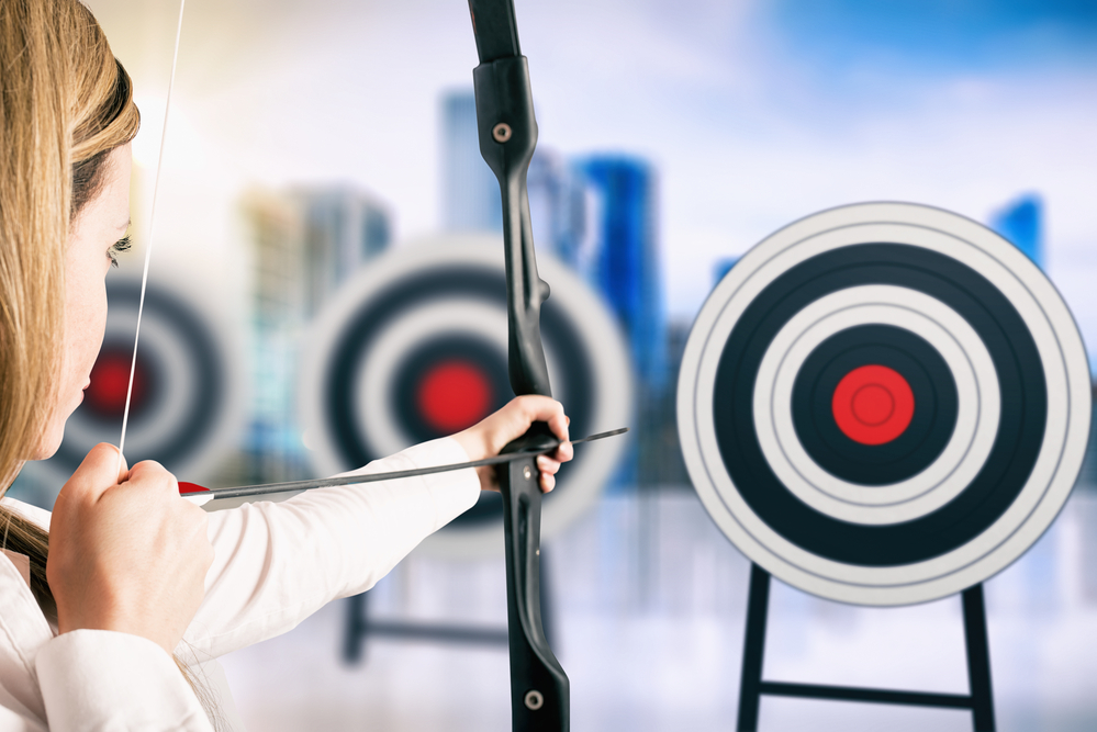 Businesswoman with bow and arrow pointing the center of the target