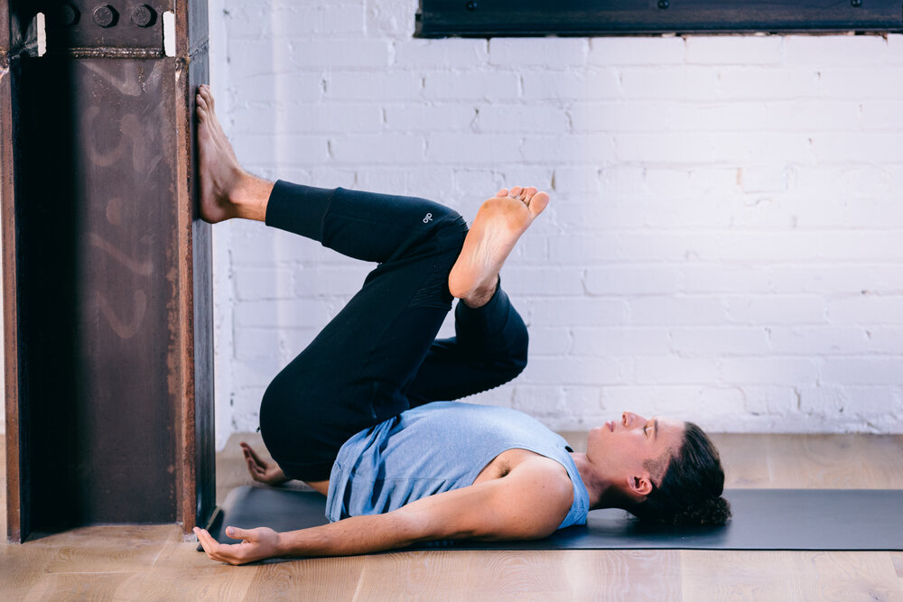 Woman on her back stretching her knees against a wall