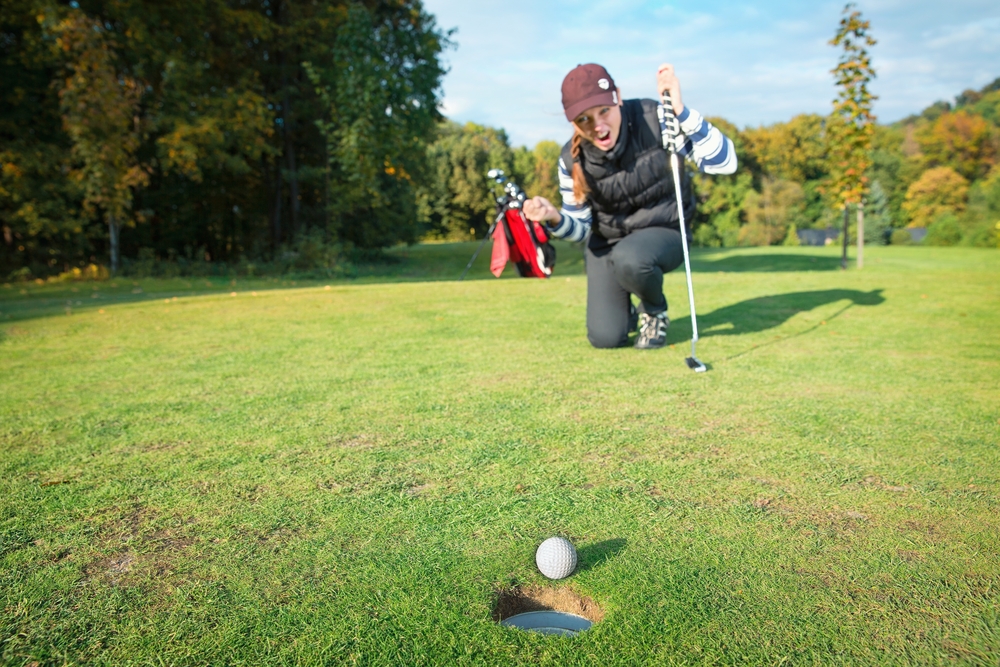 A female golfer is excited about her ball that is on the edge of the hole