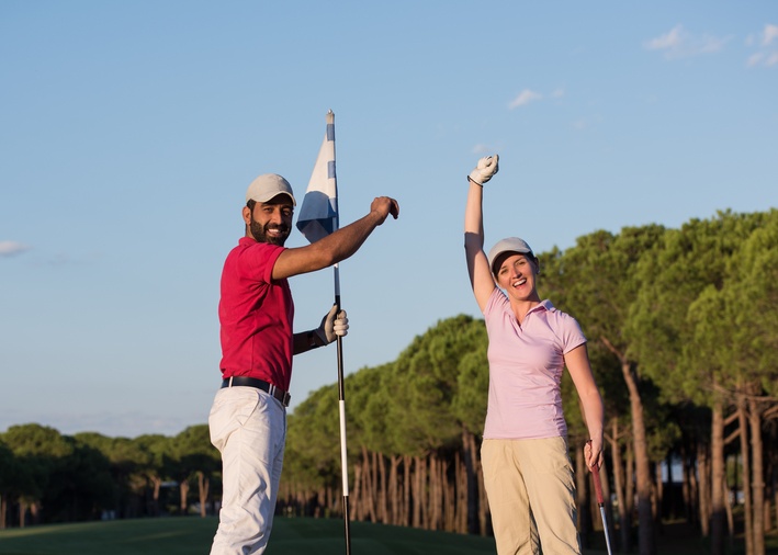 A woman is happy holding up her golf ball at the pin