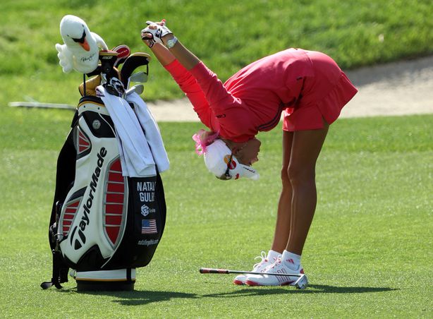 A woman bending to stretch shoulders on the golf course.