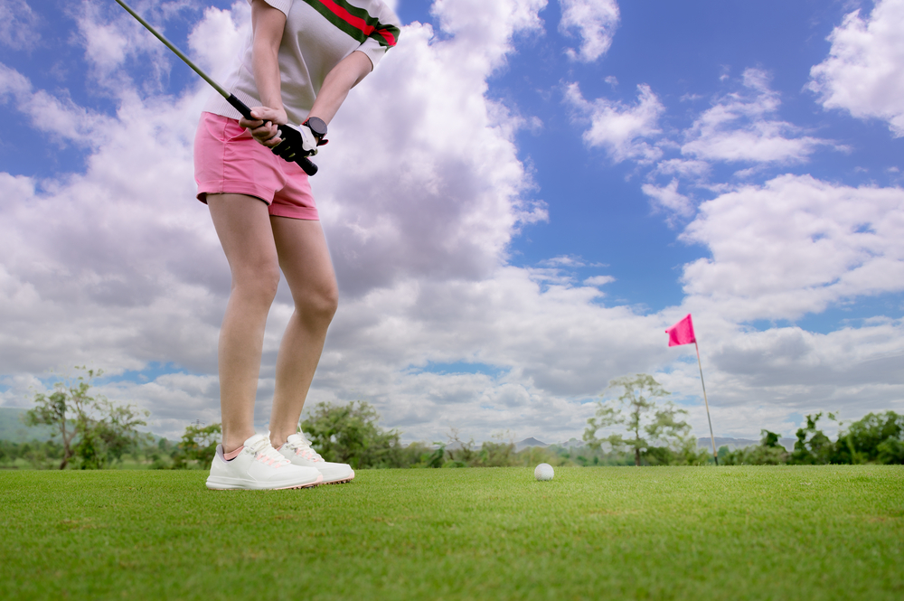 woman golf player in action of being chip golf ball from rough of fairway to the destination green at day light sky