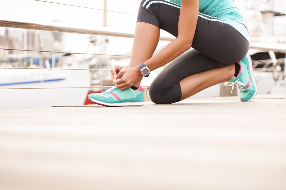 A woman bending down to prepare for a morning run on the docks.