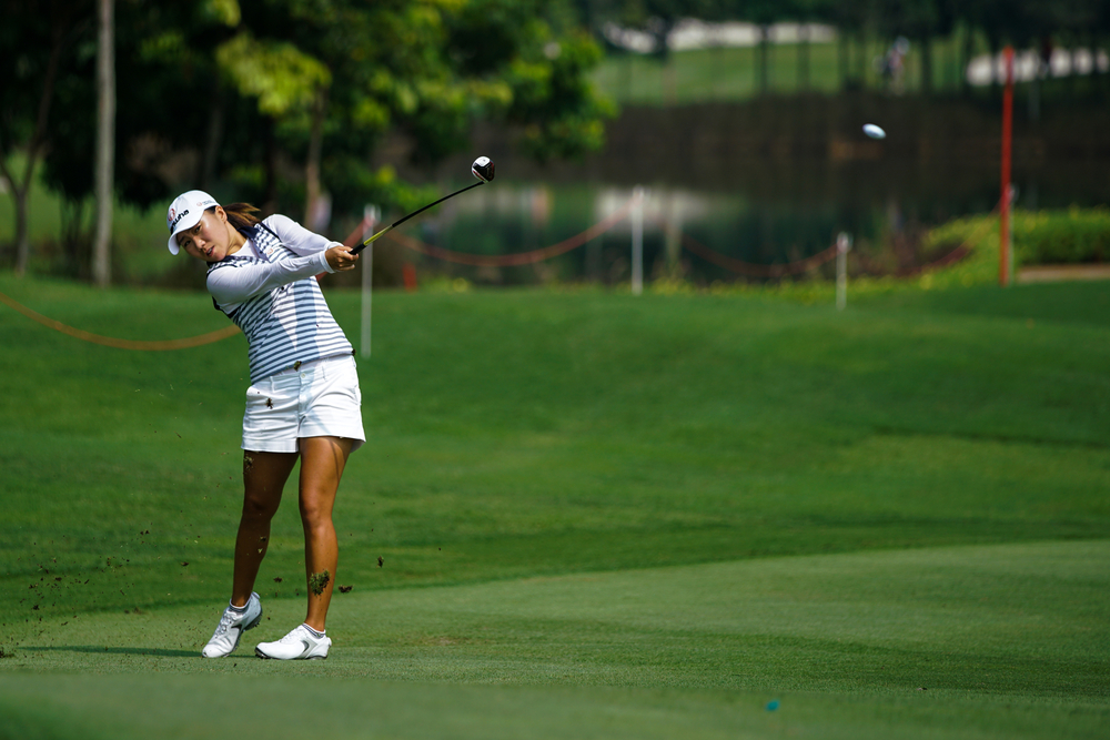 A female golfer on a tour is following through her swing.