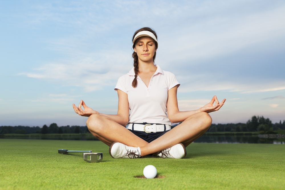 Girl golfer sitting in yoga posture on golf course.