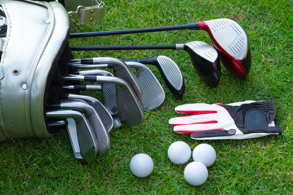 Golf clubs, golf balls, and a glove arranged on green grass beside a golf bag, symbolizing preparation, patience, and trusting the journey of improvement in golf."