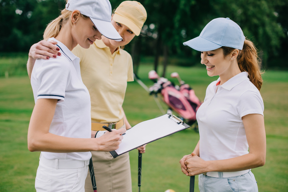 Three women golfers reviewing a scorecard and discussing their scores during a round of golf.
